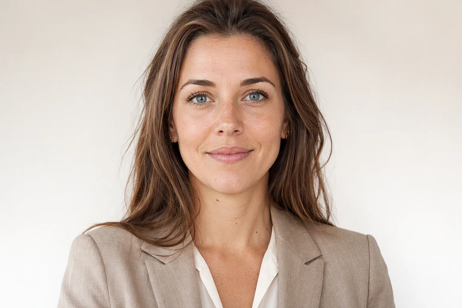 Vrouw met halflang bruin haar in beige blazer en witte blouse, zakelijk portret